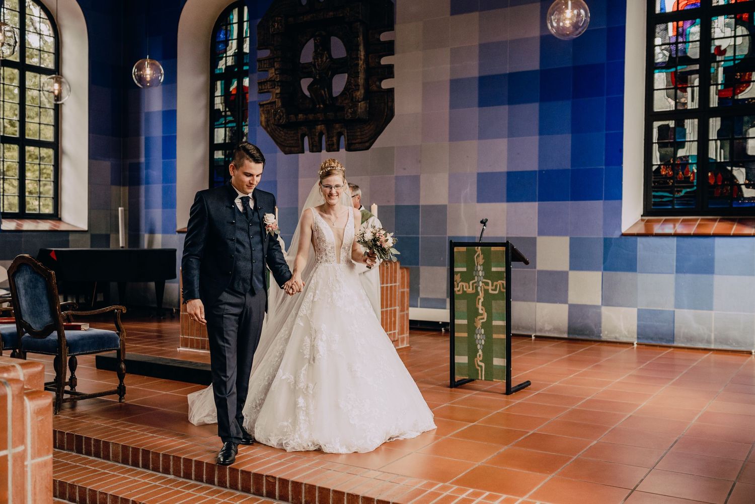 A couple standing together in a church with blue tiled walls and arched windows during their wedding ceremony.