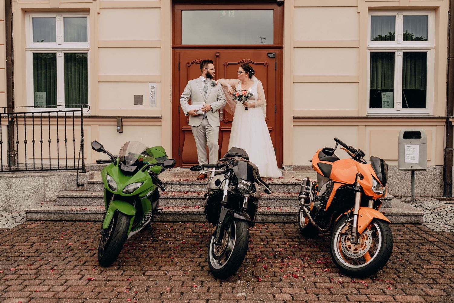 Row of colorful motorcycles parked along a cobblestone street beside a beige building wall with windows.