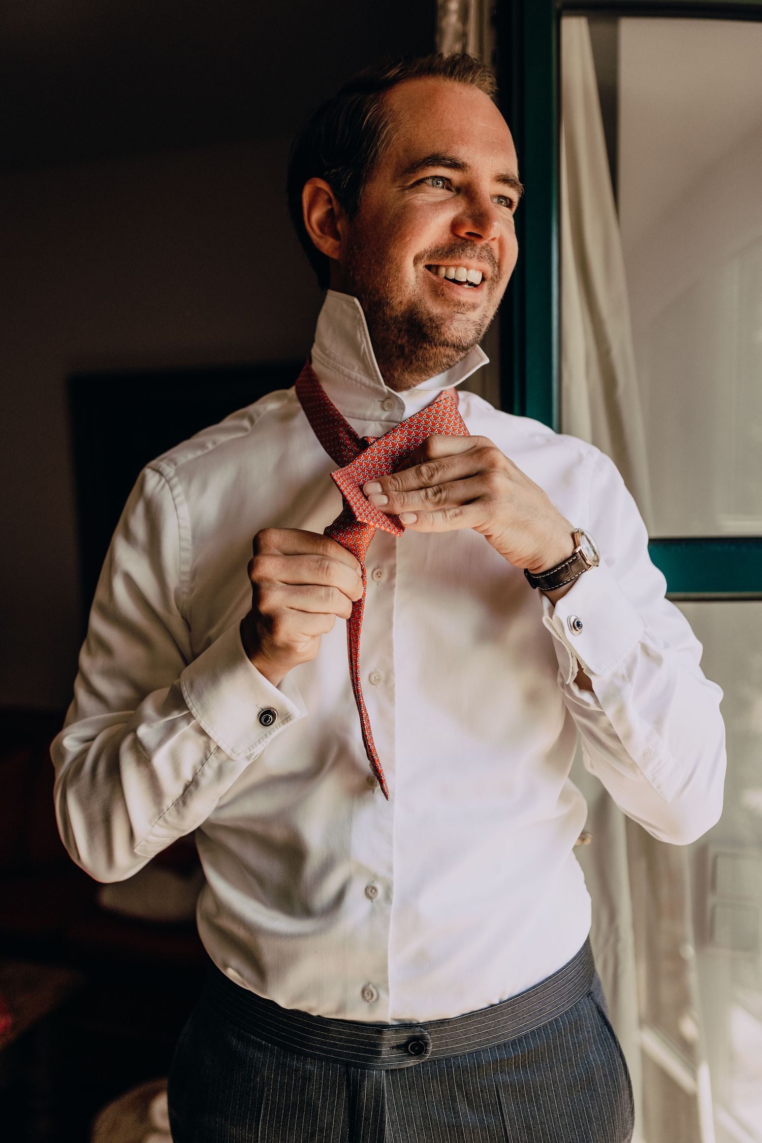 Person adjusting a coral-colored bow tie while wearing a crisp white dress shirt.