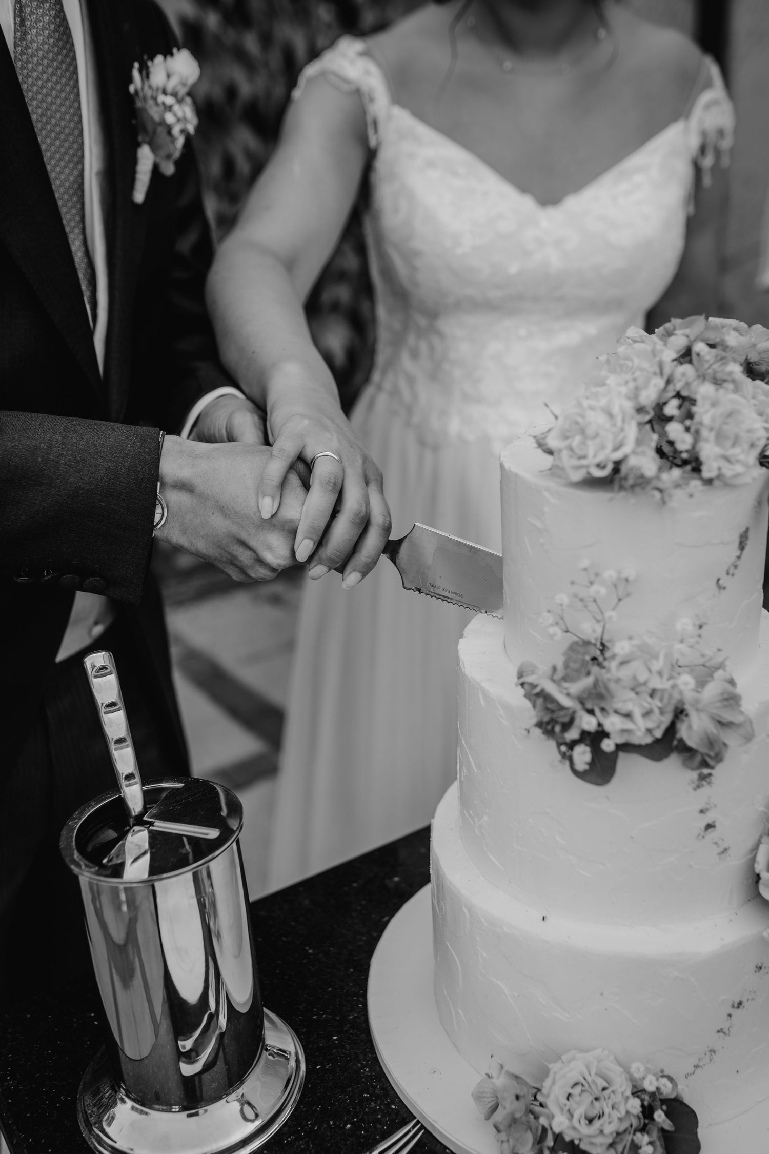Black and white photo of wedding cake cutting with floral decorations.