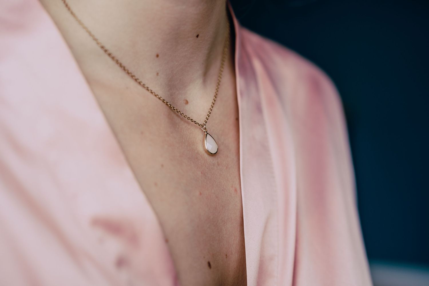 Delicate necklace and soft pink fabric detail in elegant wedding attire.