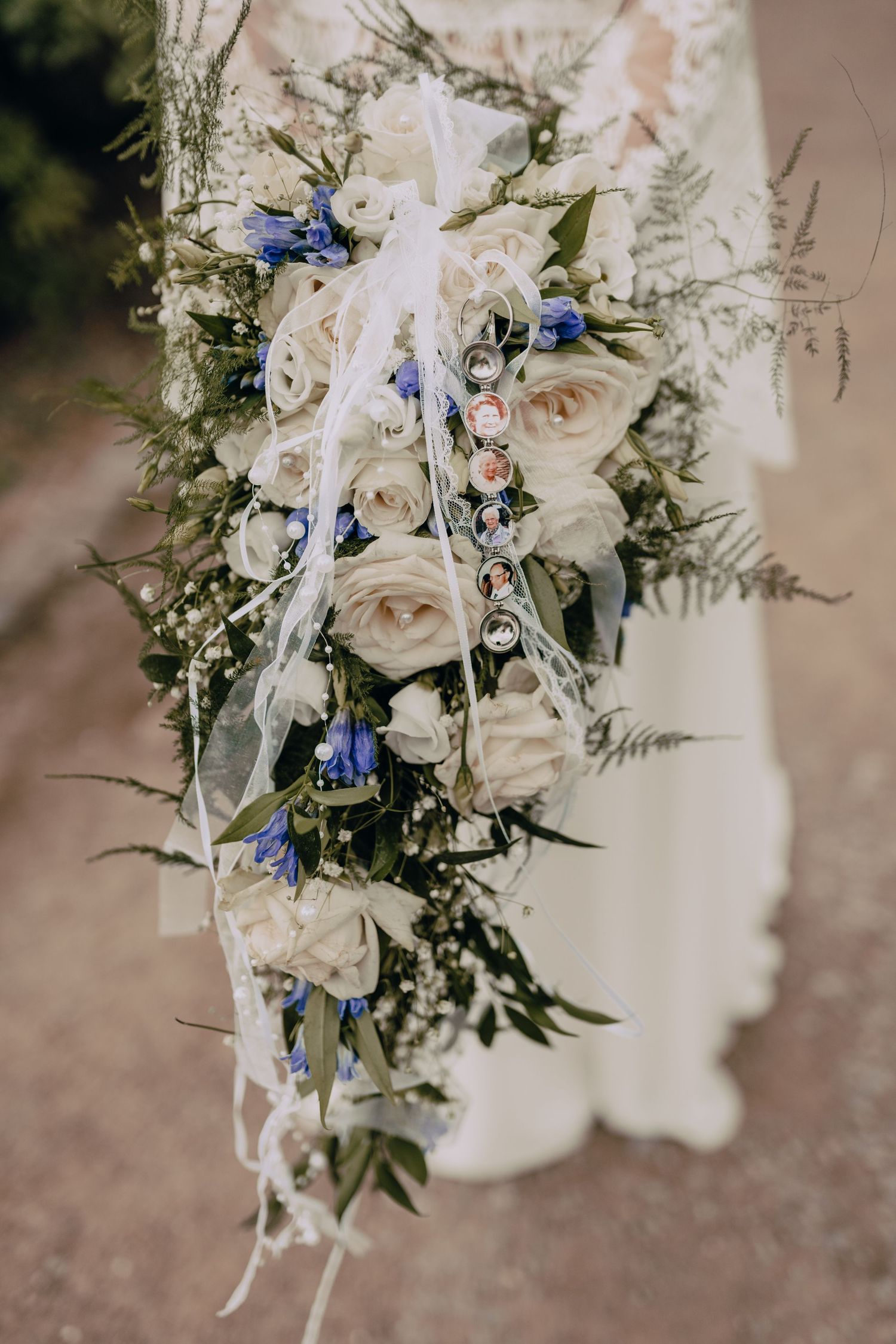 A cascading bridal bouquet featuring cream roses and blue delphinium flowers with delicate greenery and white ribbons.