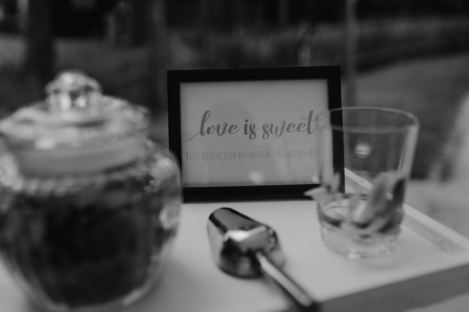 Black and white photo of a 'Love is Sweet' sign display next to dessert settings.