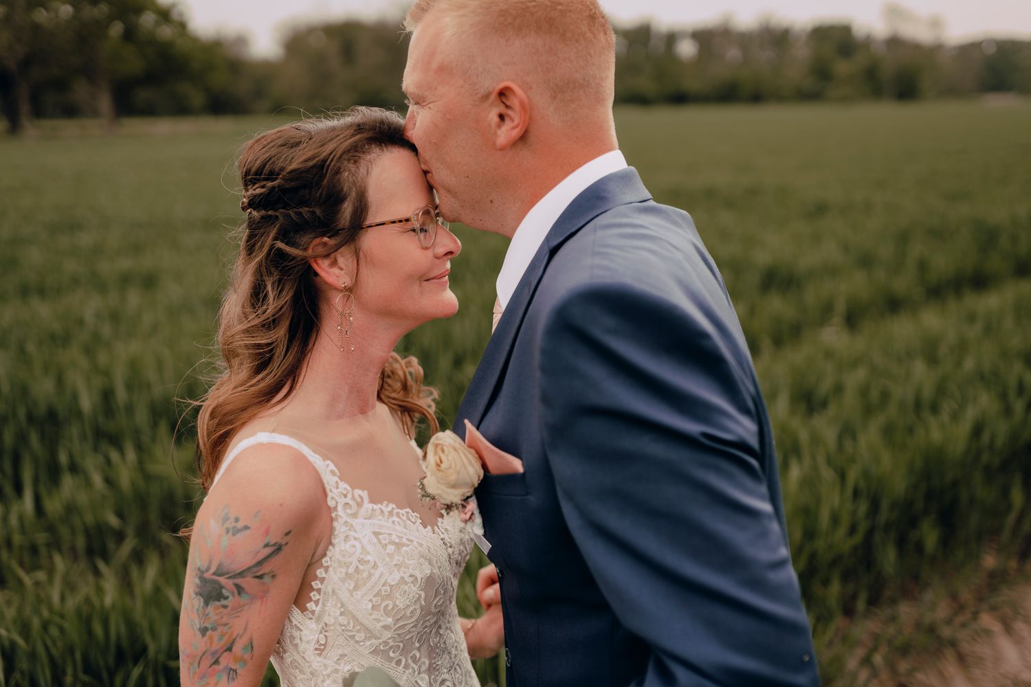 A romantic couple embraces in a lush green wheat field on a sunny summer afternoon, creating an intimate wedding moment.