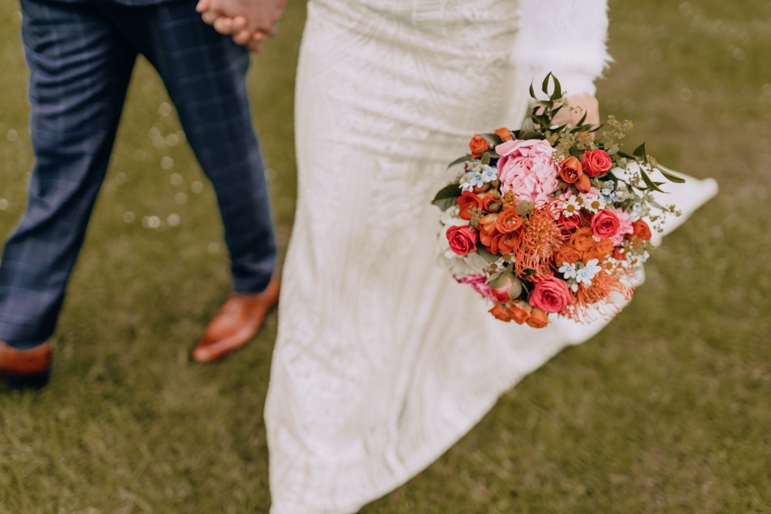 Close-up of a bride holding a vibrant pink and coral wedding bouquet against her white dress.