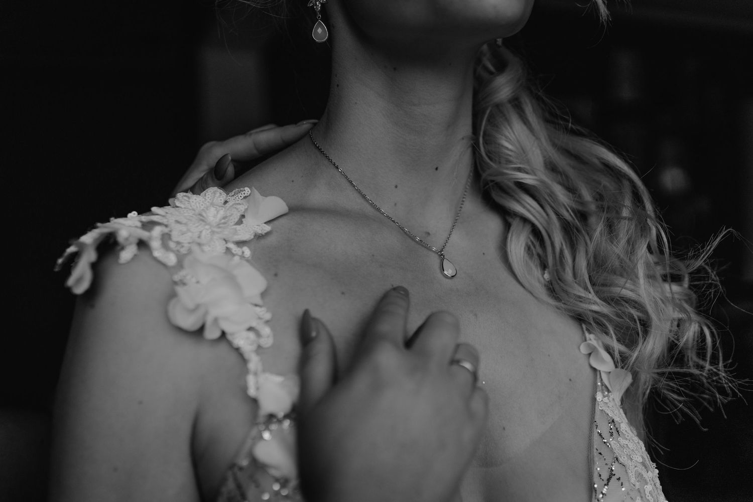 Black and white detail shot of lace wedding dress bodice and delicate necklace.