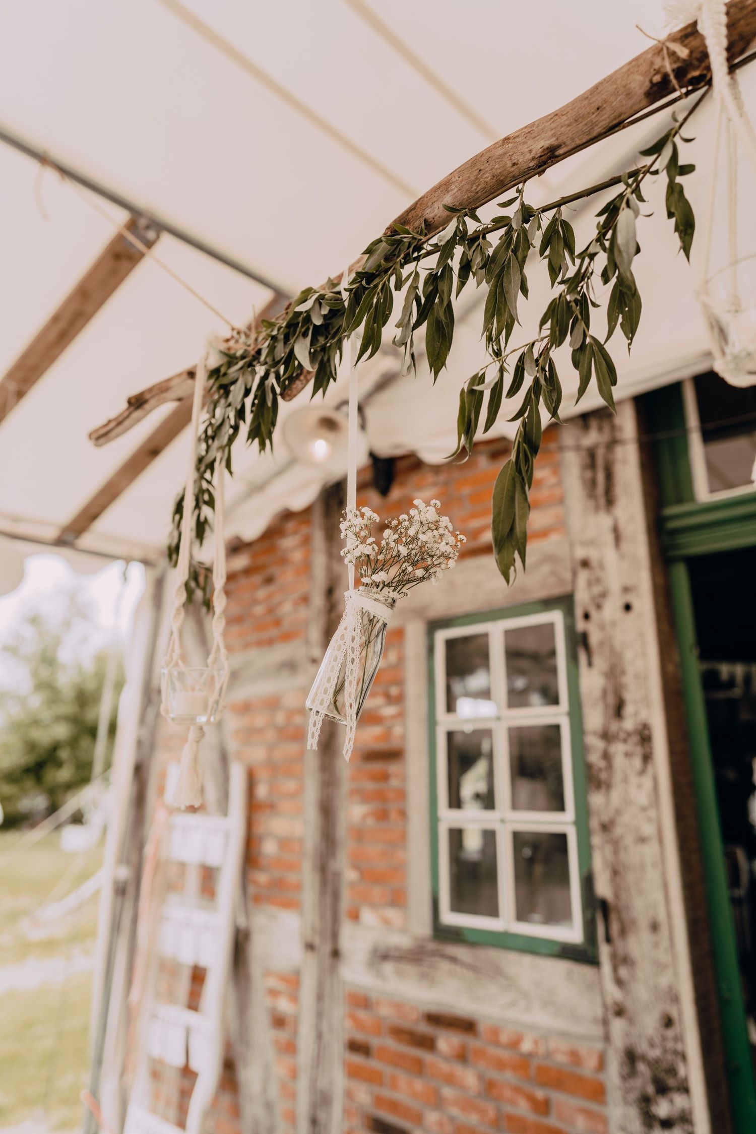 Rustic brick cottage decorated with hanging eucalyptus branches and glass ornaments for an outdoor wedding celebration.