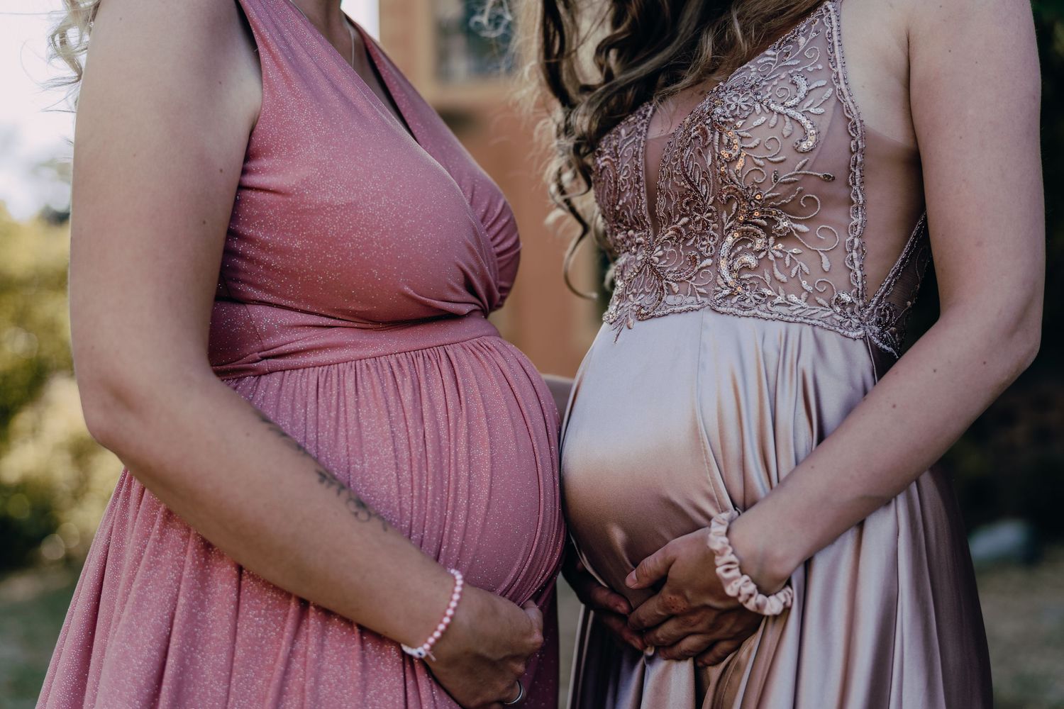 Two bridesmaids in mauve and blush gowns standing together showing their dresses.