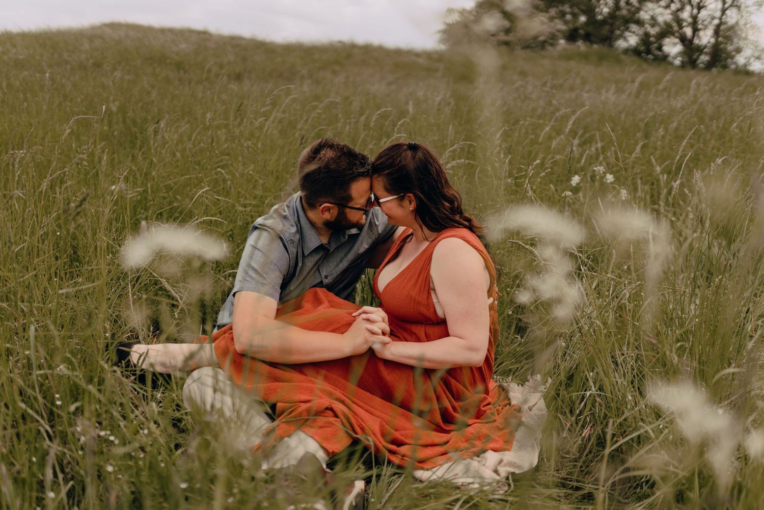 A natural outdoor setting showing intimate embraces in a sunny field with grass and trees in the background.