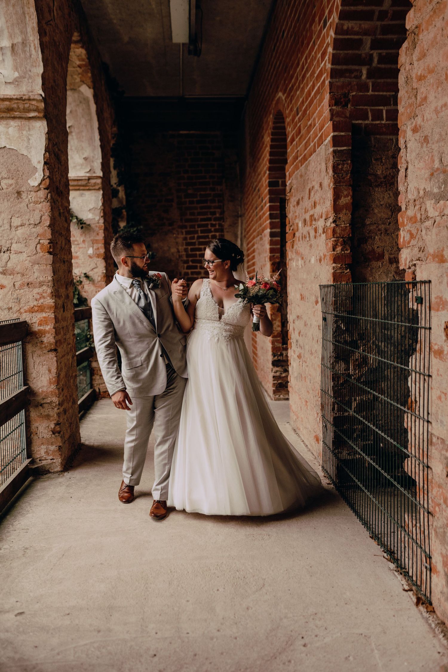 Wedding couple shares intimate moment in rustic brick hallway setting.