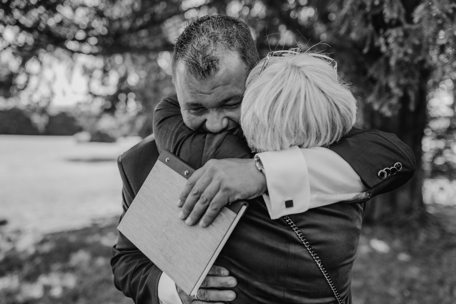 An emotional moment captured in black and white as two people share a tender embrace while reading a letter outdoors.