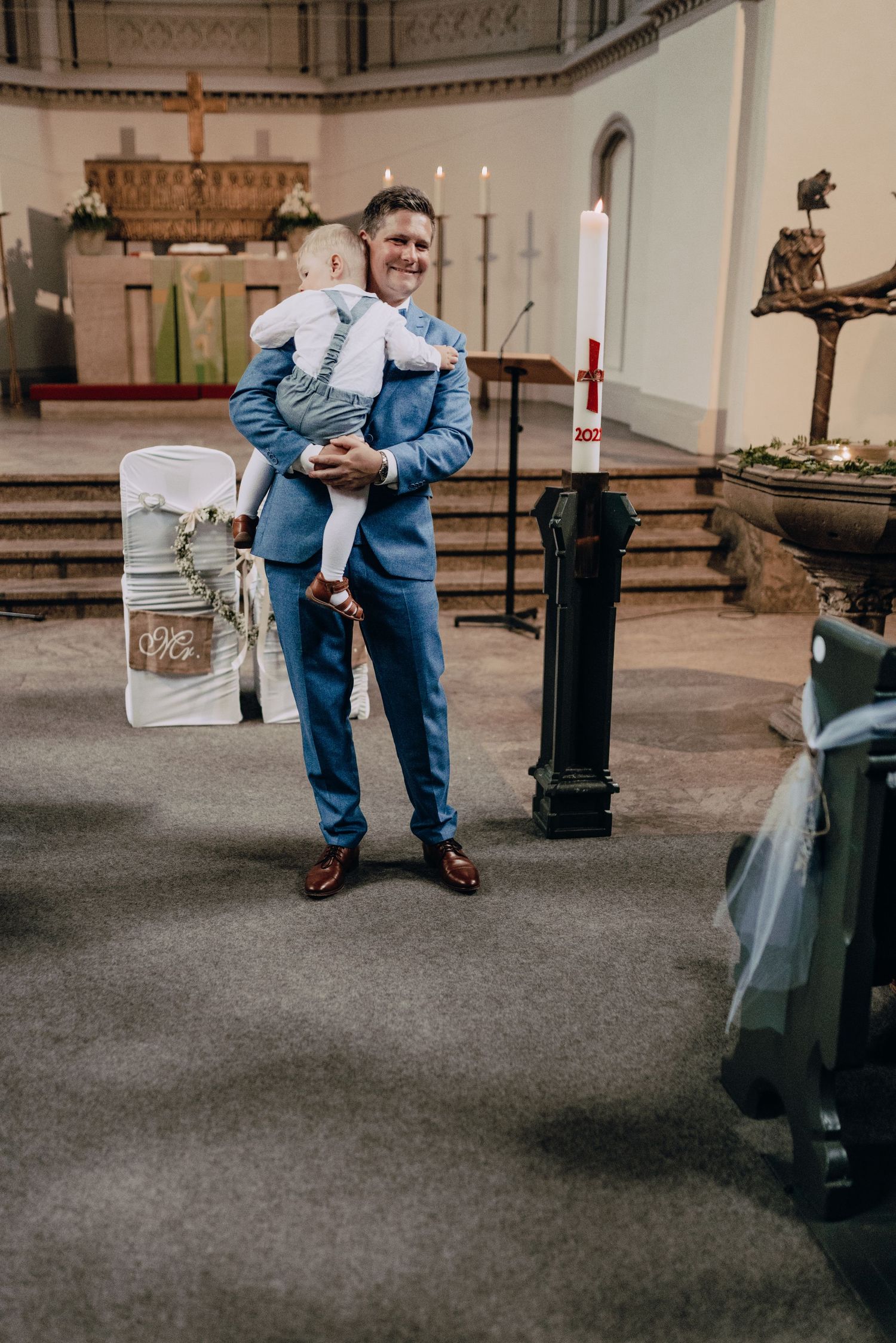 A well-dressed pair stand inside a church interior with architectural details and decorative elements visible.