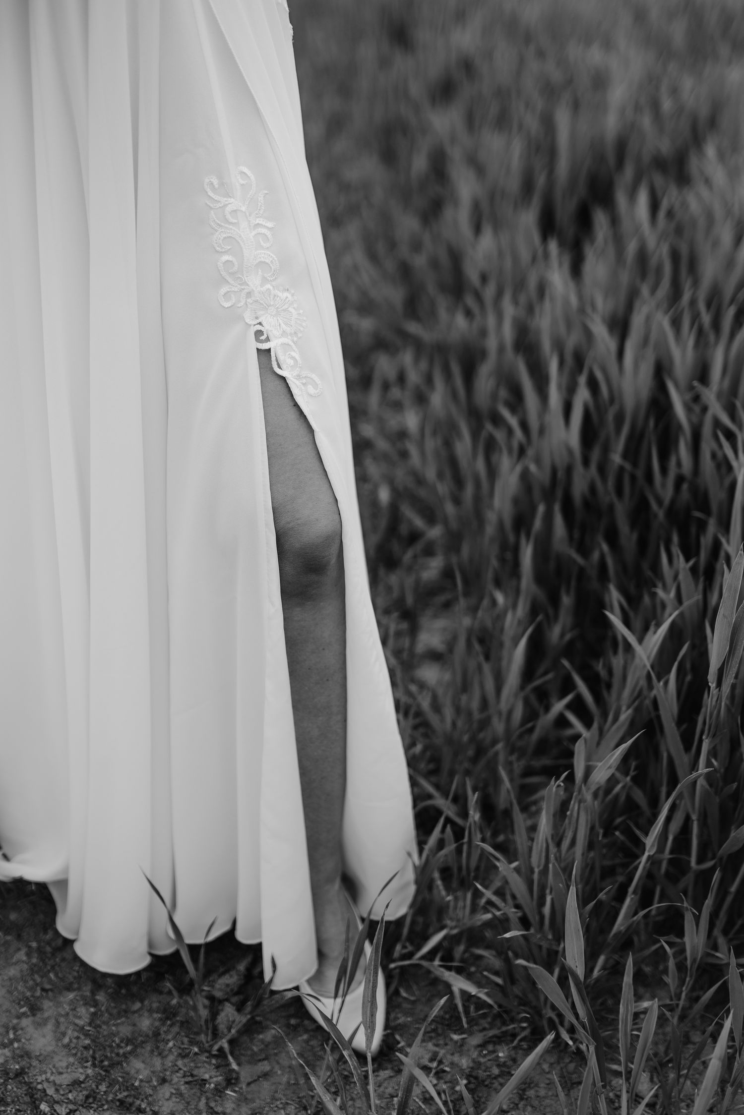Detail shot of delicate white wedding dress embroidery against tall grass in black and white.