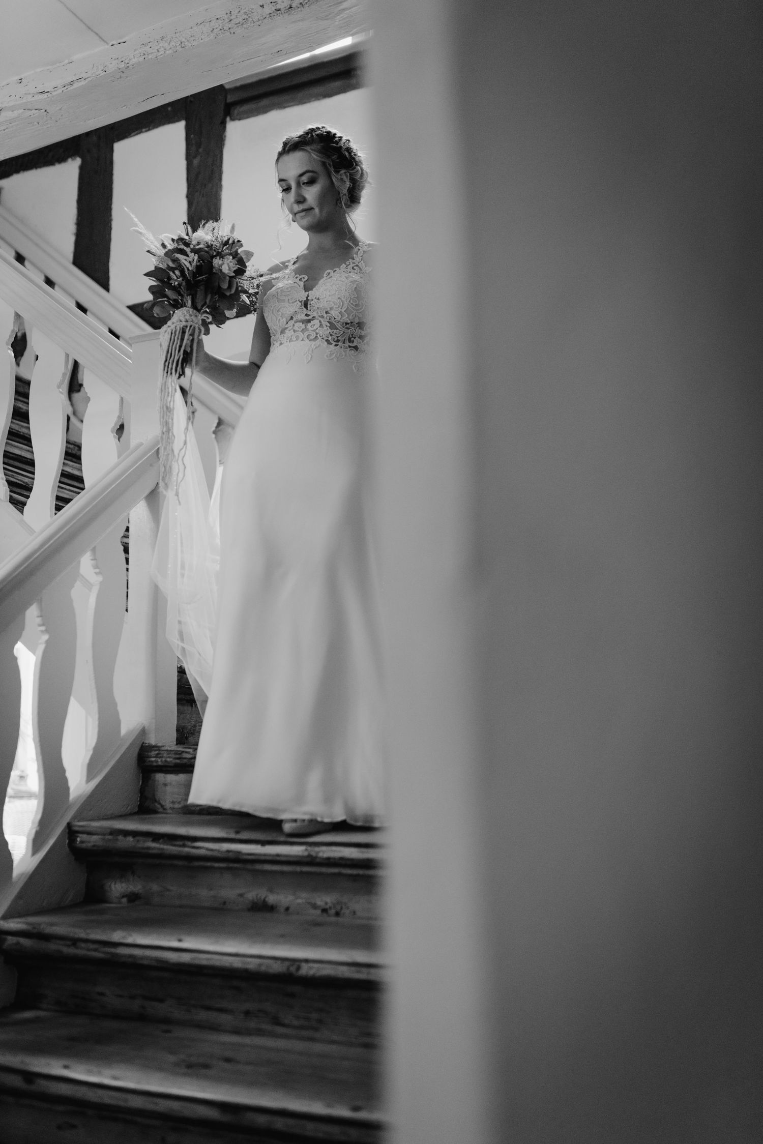 A bride in an elegant white wedding dress stands on a staircase holding a bouquet in black and white.