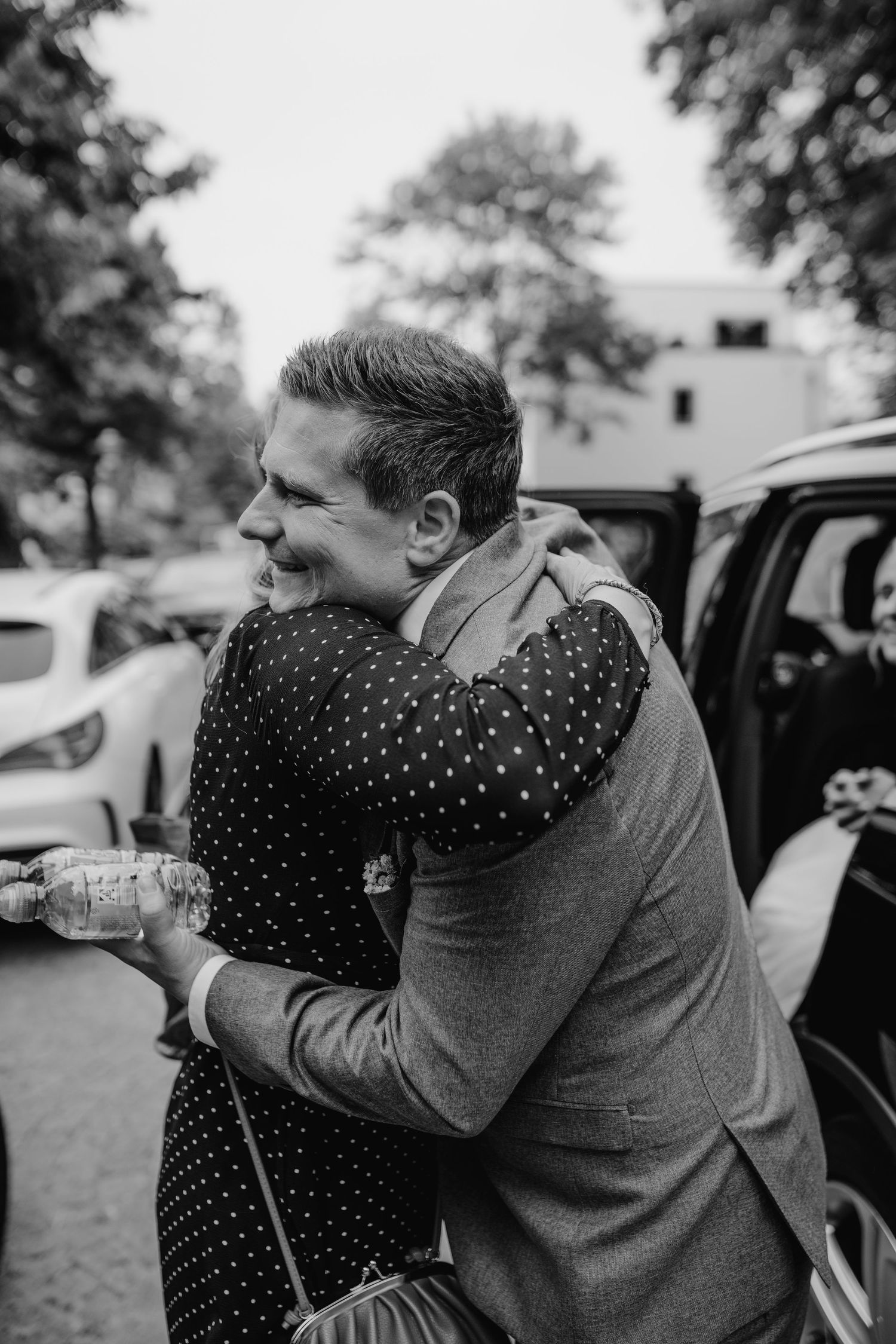A heartfelt sequence of two people embracing outdoors next to a car in black and white photography.