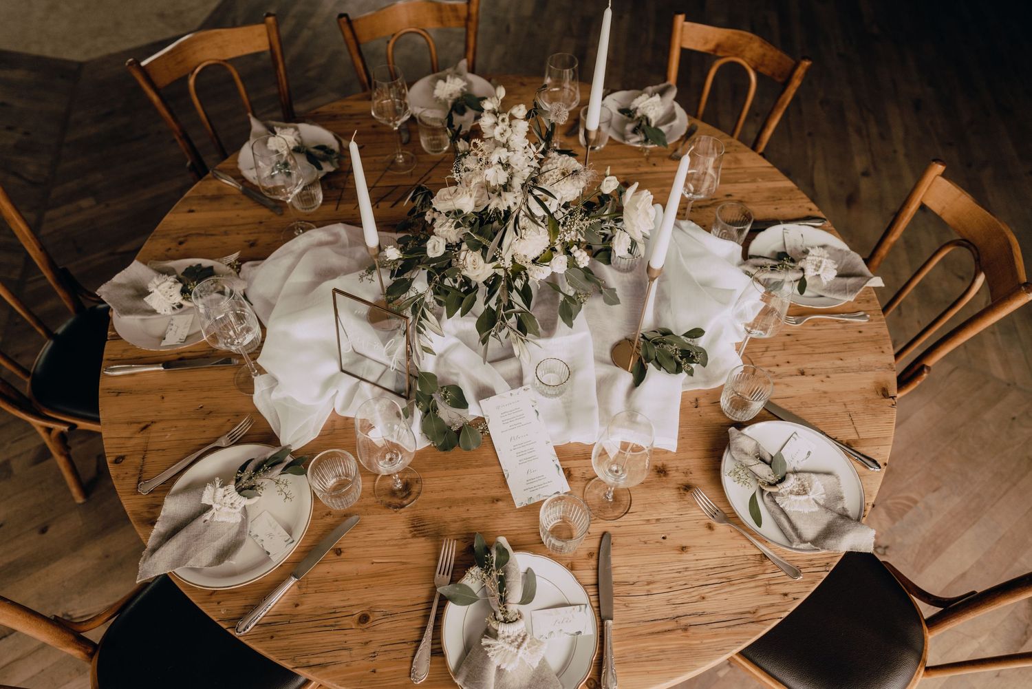 Elegant wedding table setting with white candles and floral centerpiece on rustic wooden round table.