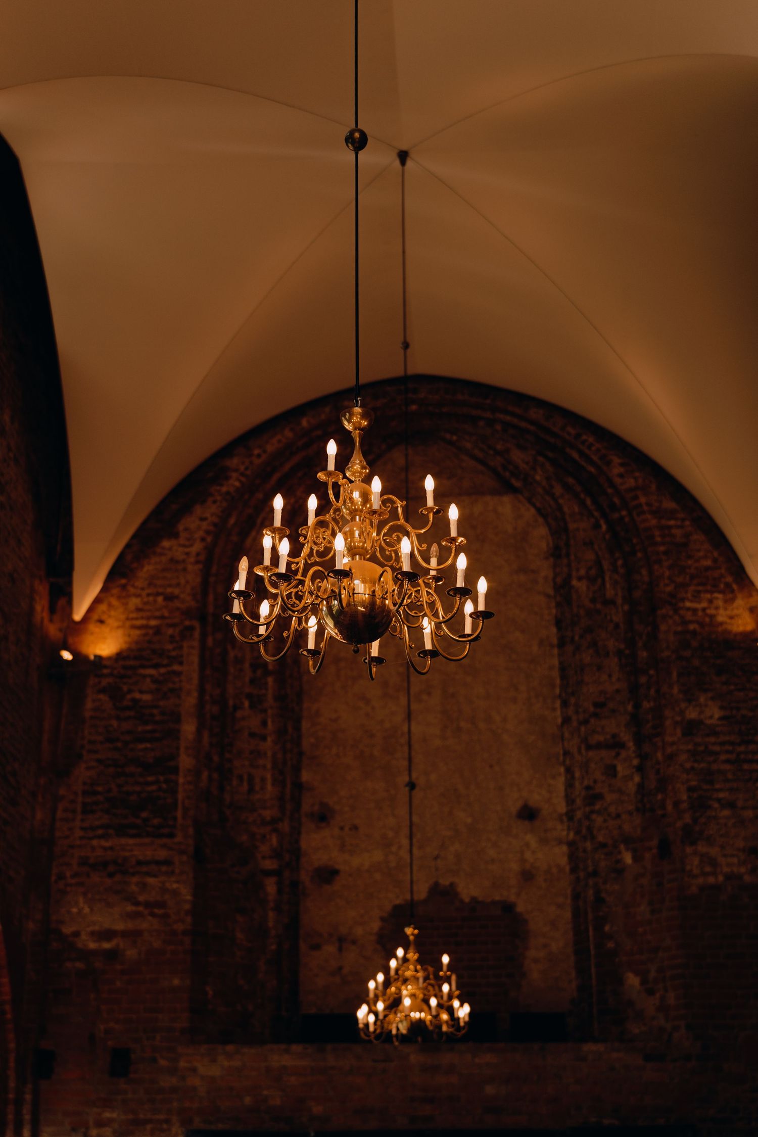 An elegant crystal chandelier hangs in an arched brick venue with warm ambient lighting.