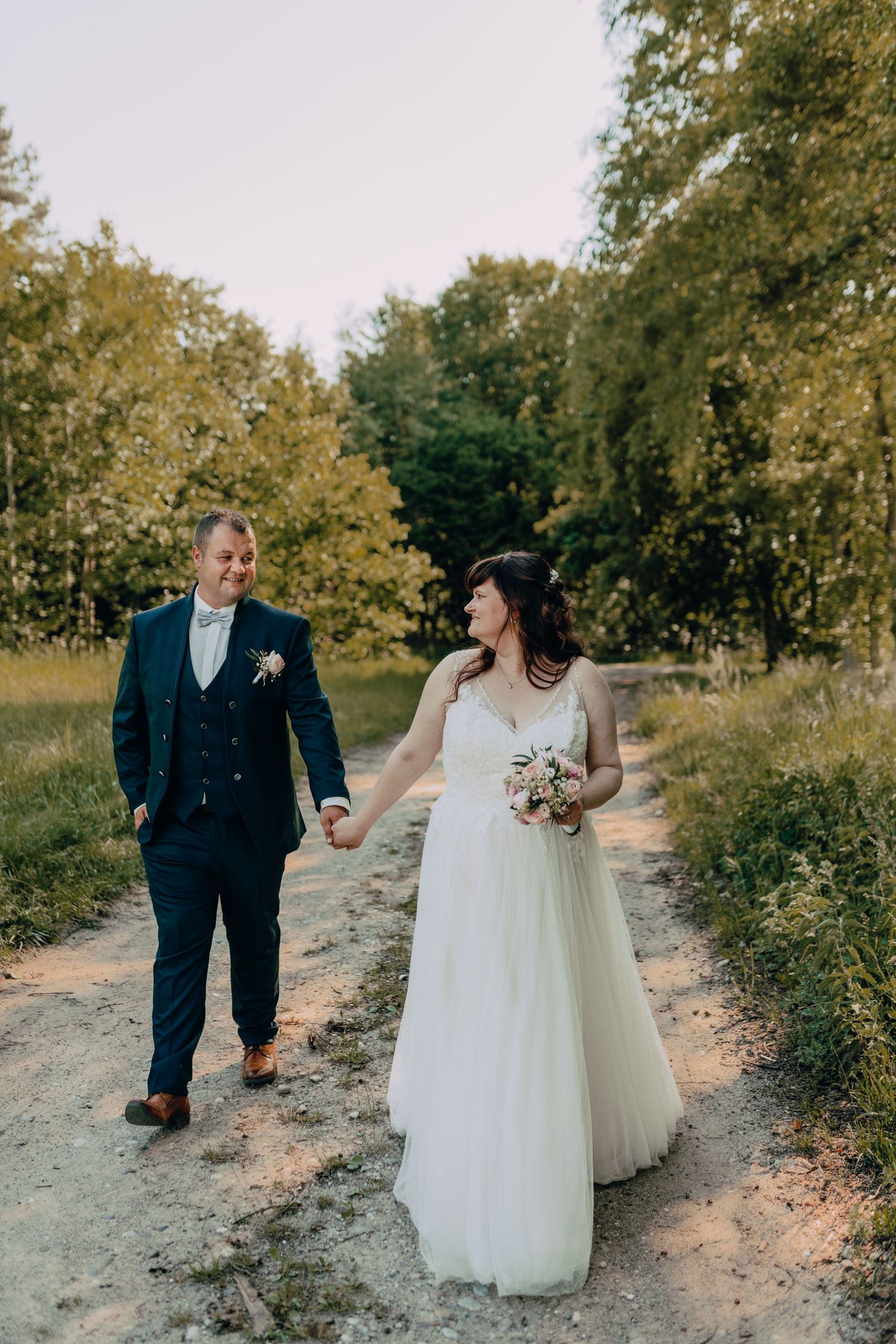 Newlyweds strolling along a sandy path surrounded by lush greenery on their wedding day.