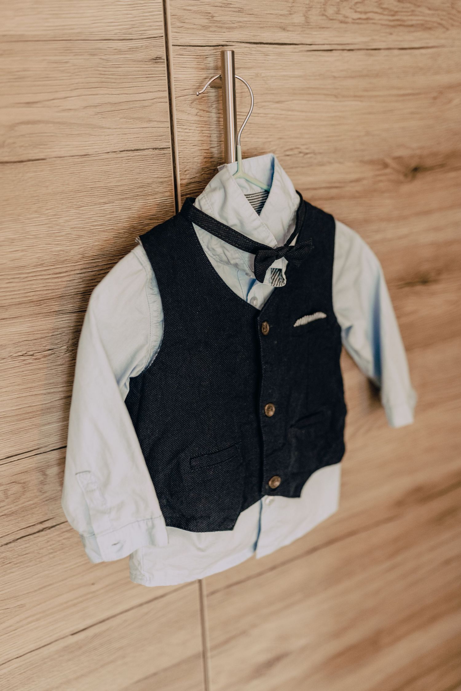 A stylish navy blue vest and white dress shirt hanging on a wooden wall, perfect for formal children's attire.