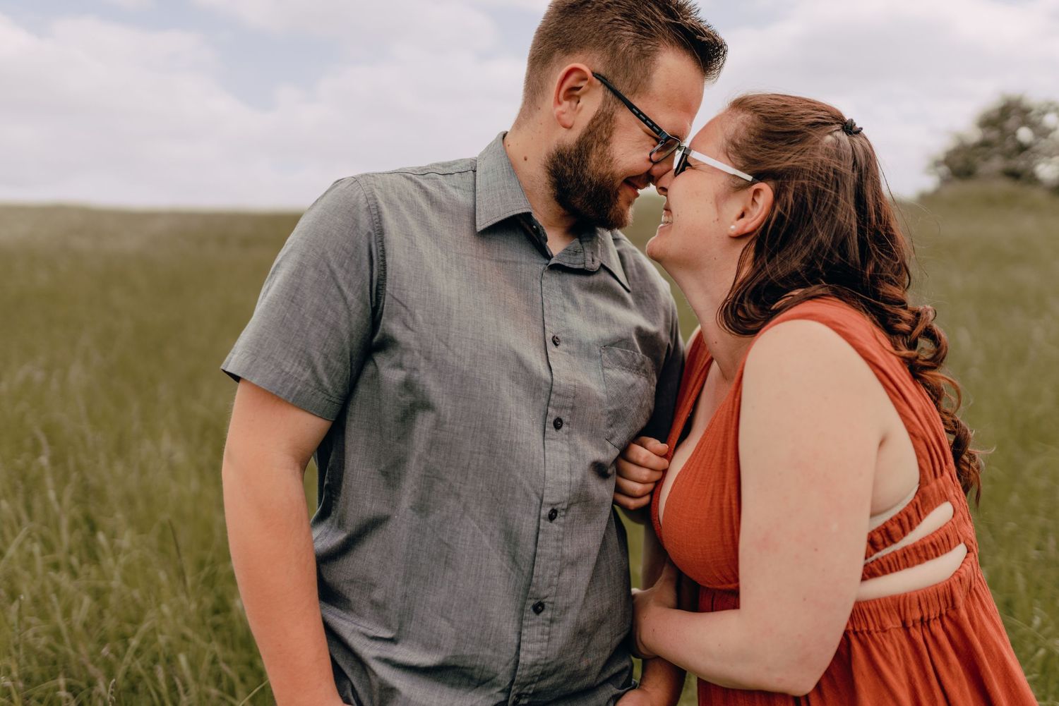 A couple shares an intimate moment together while standing in a green grassy field on an overcast day.