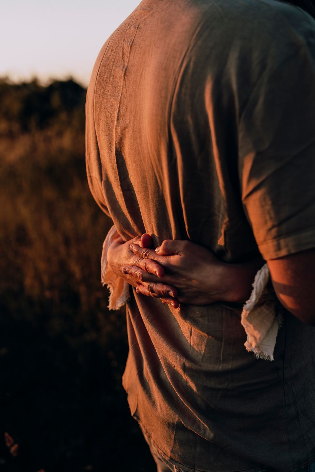 Close-up view of hands grasping fabric of a shirt against warm sunset lighting in a field.