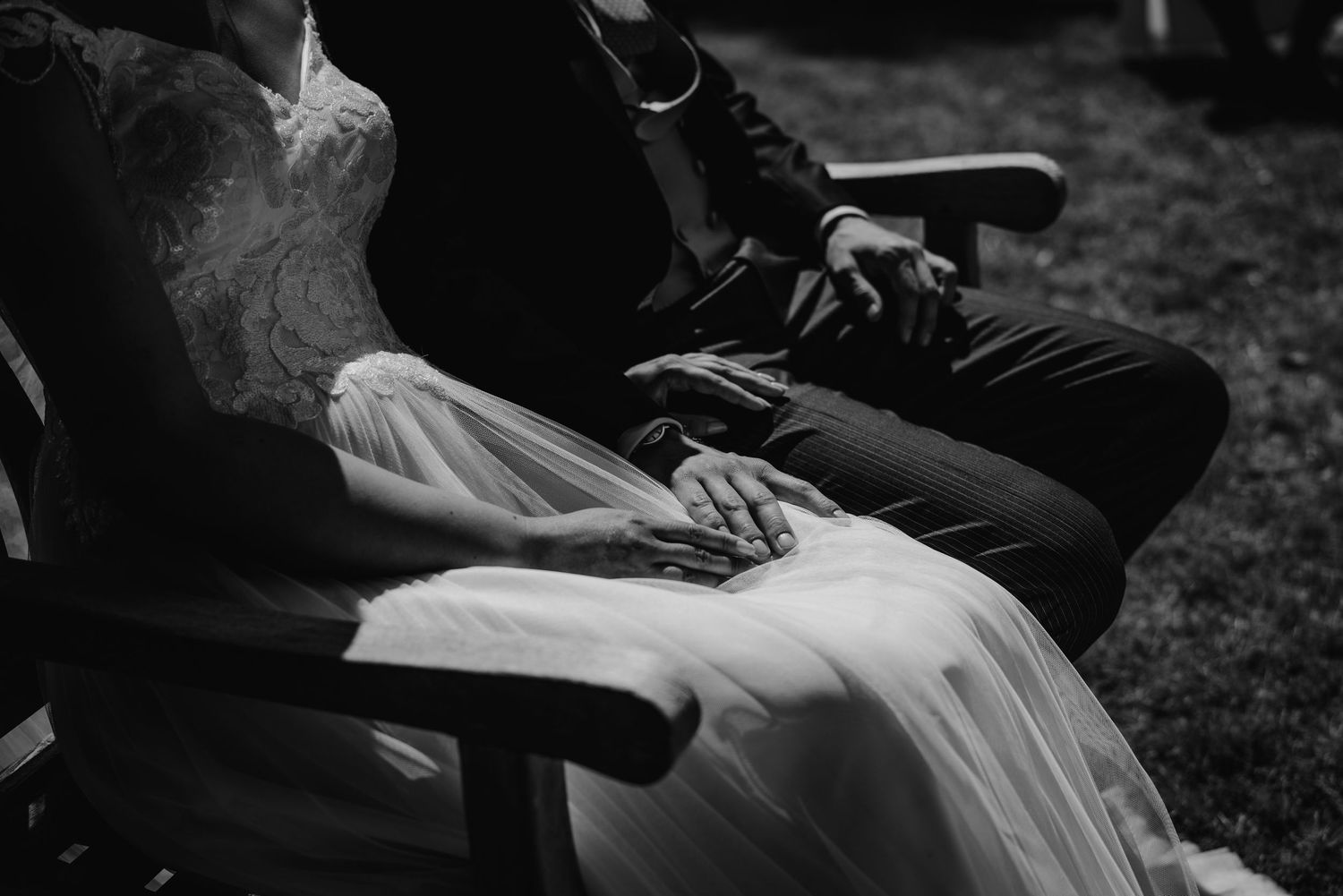 Black and white detail shot of hands resting on white wedding dress fabric.