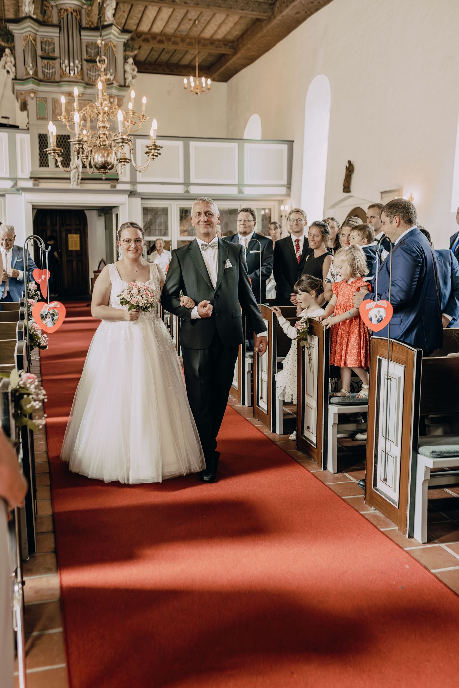 A church wedding ceremony showing guests seated in pews as the bride walks down the red-carpeted aisle.