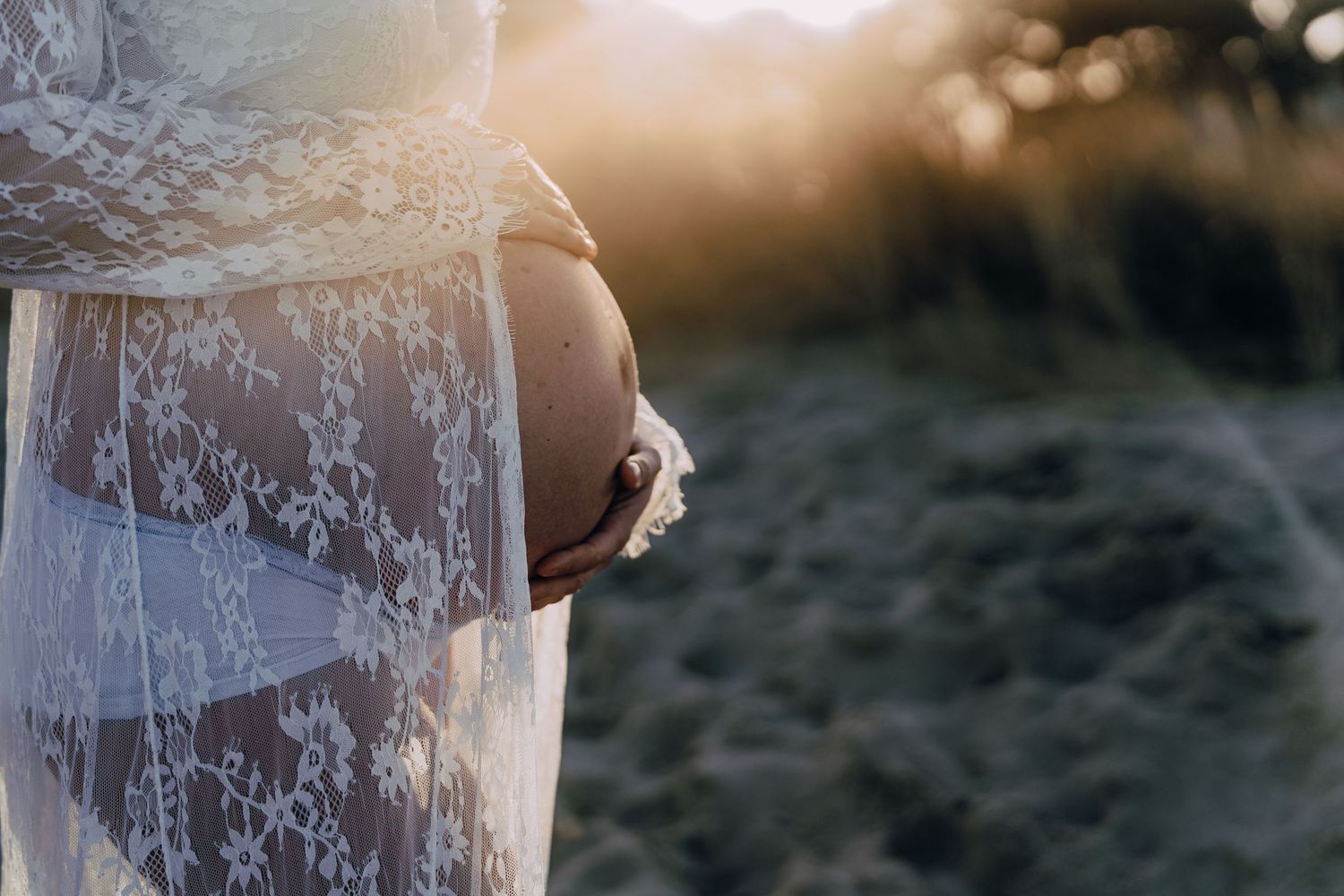 Beautiful delicate white lace dress detail captured in golden sunlight during an outdoor sunset photoshoot.