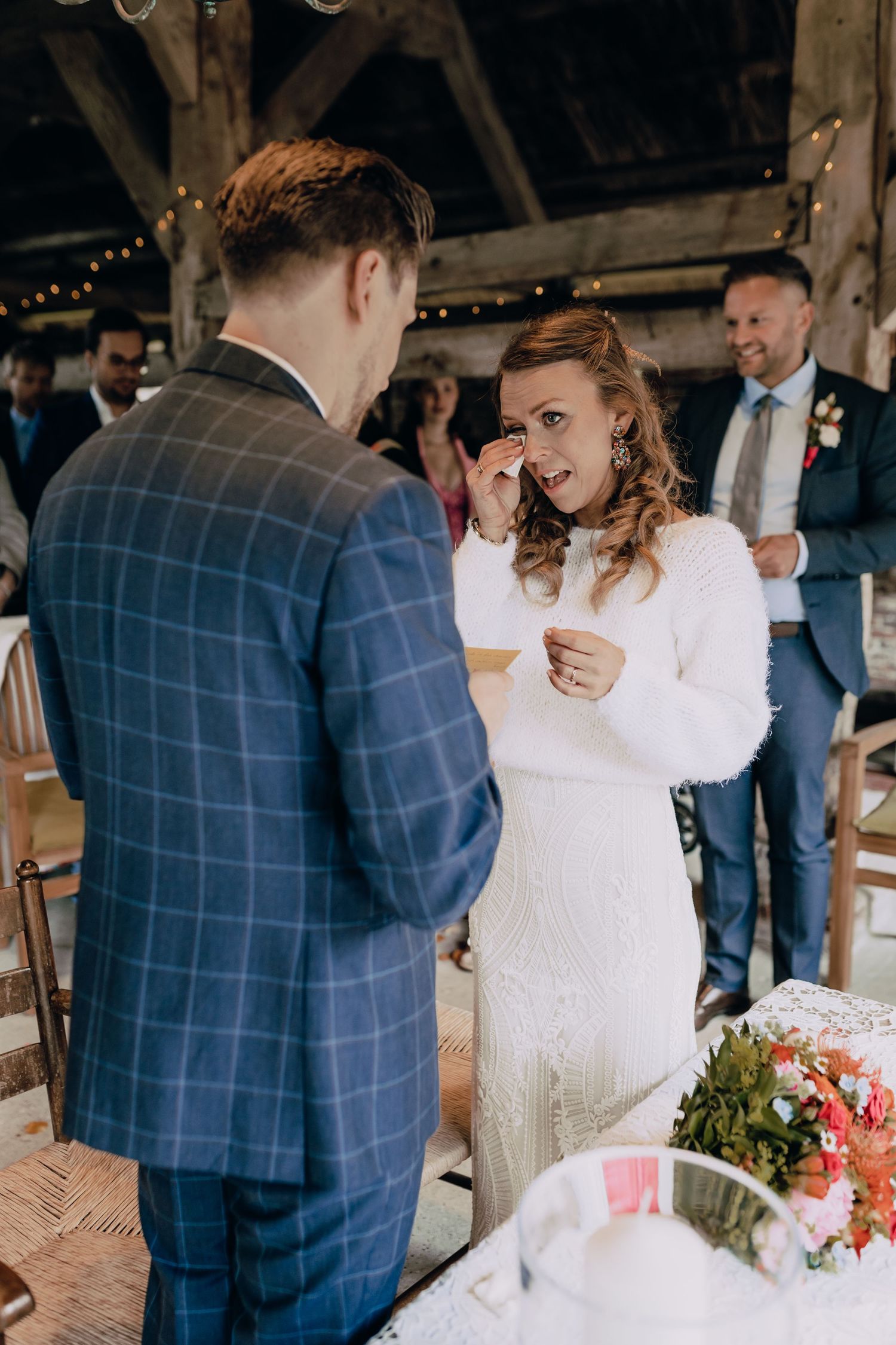 Wedding couple sharing a moment in a rustic barn setting with guests in background.