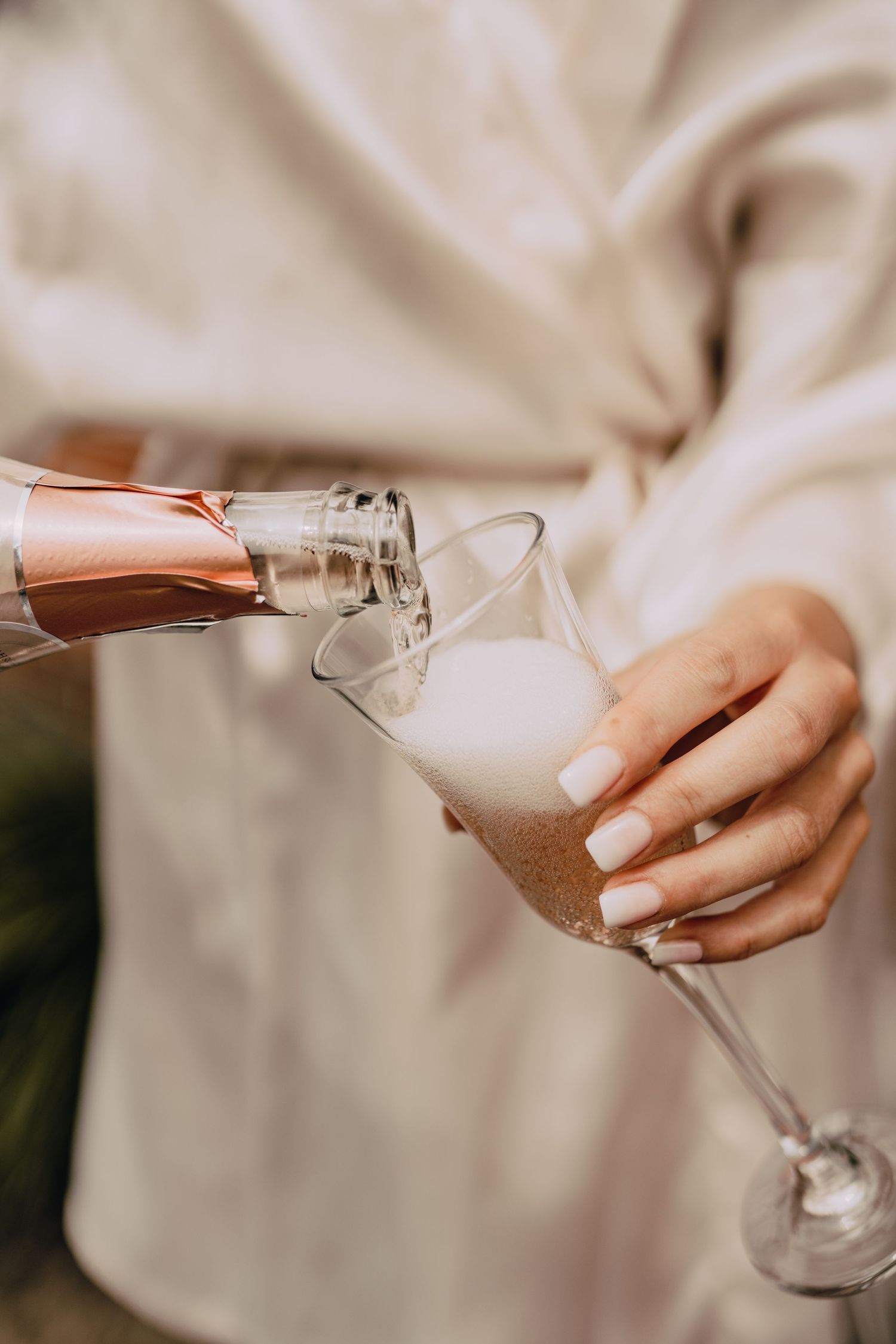 Hands pouring champagne into elegant glassware during wedding preparations.