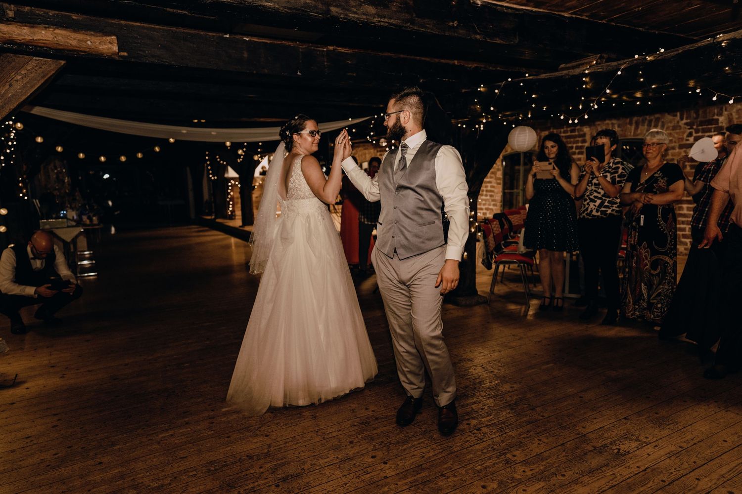Wedding celebration in rustic venue with string lights and wooden beams.