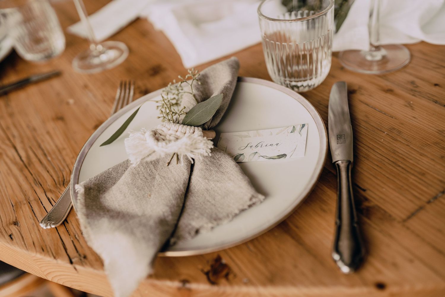 Wedding place setting with linen napkin, white plate and silverware on wooden table.