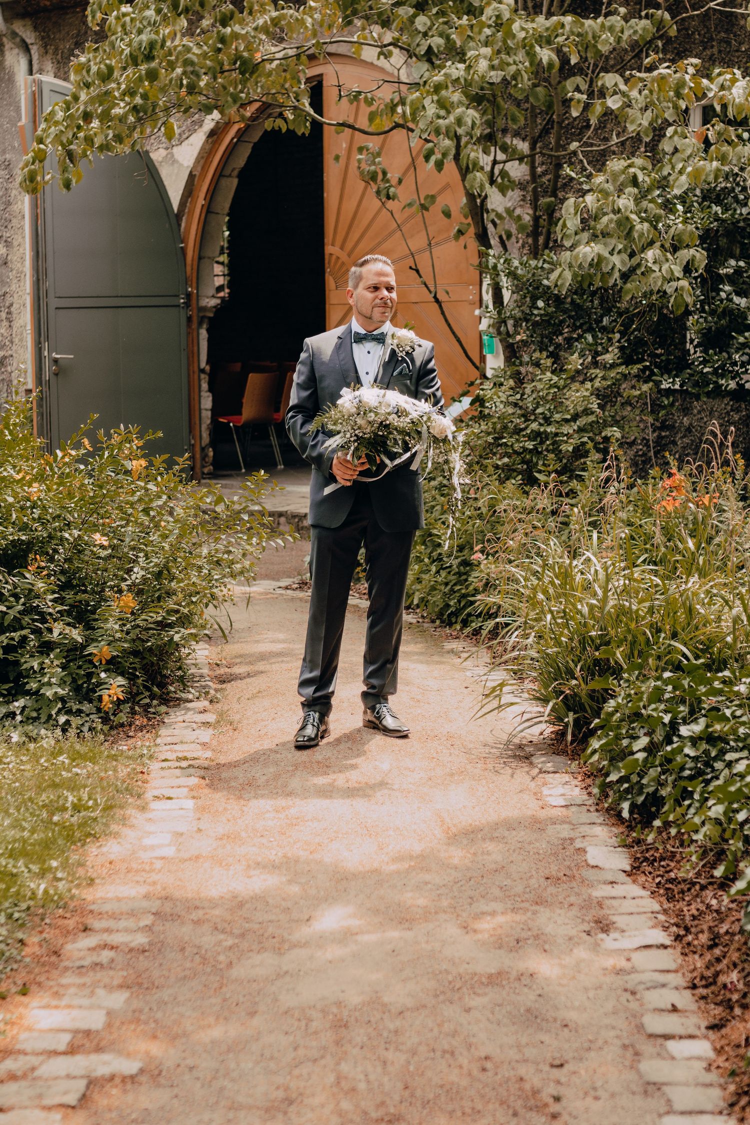 A garden path lined with greenery and white flowers leading to a doorway.