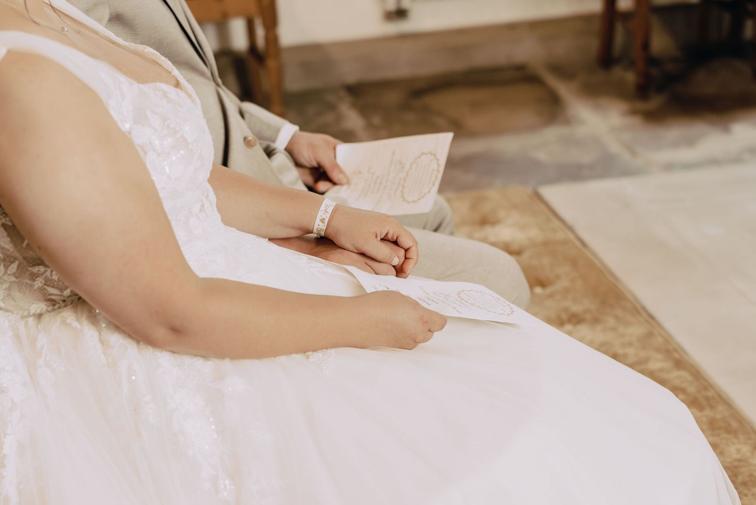 Someone in a white lace wedding dress writes with a pen on paper during wedding preparations.