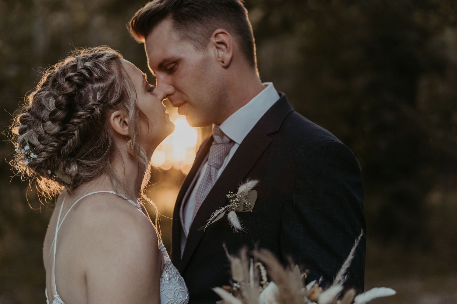 A romantic couple embraces during a sunset outdoor photoshoot against a dark natural backdrop.