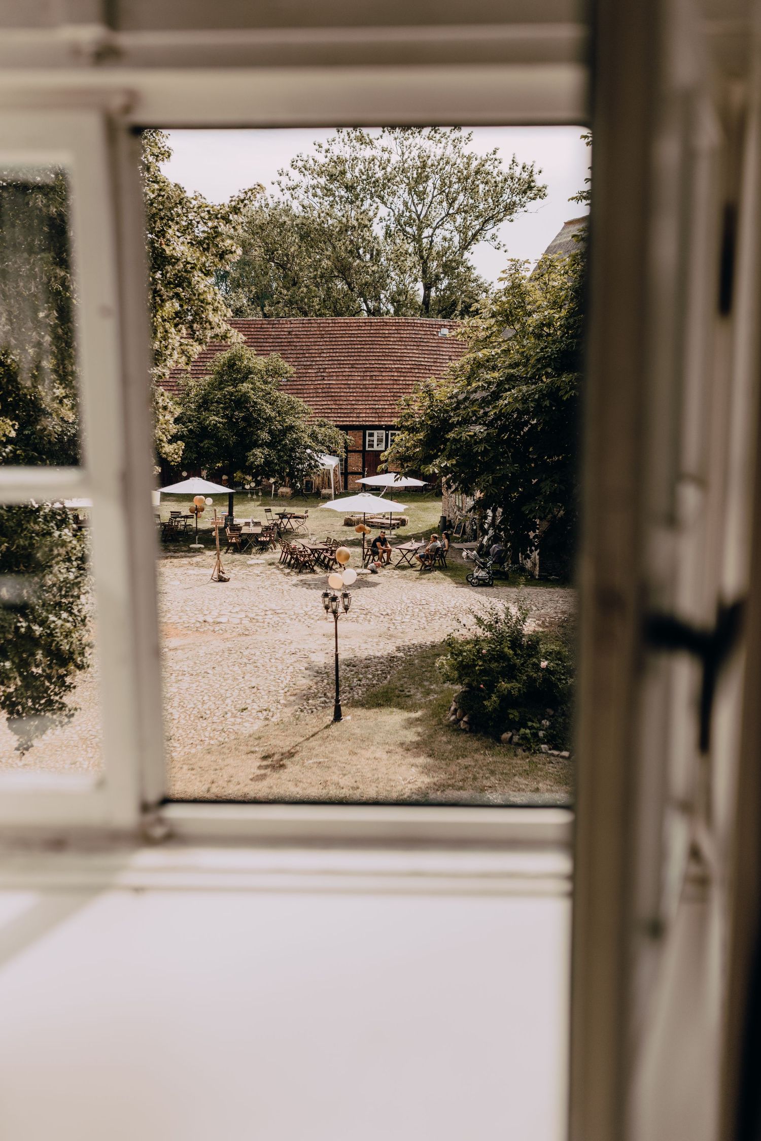 View through window panes of a rustic outdoor garden courtyard with white pillars and gravel paths.