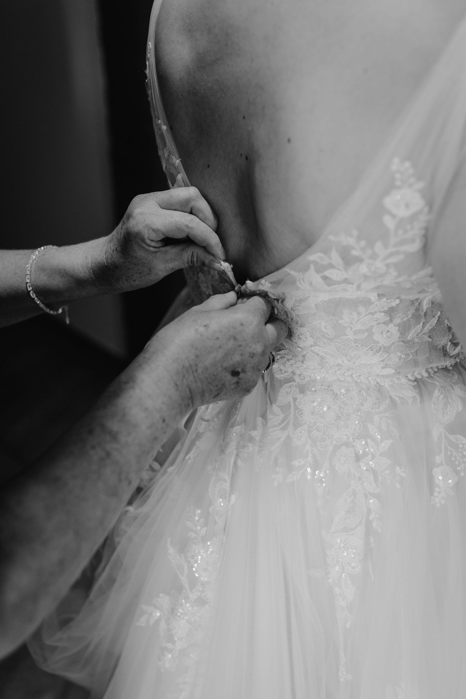 Hands lacing up the back of a detailed white lace and tulle wedding dress during bridal preparations.