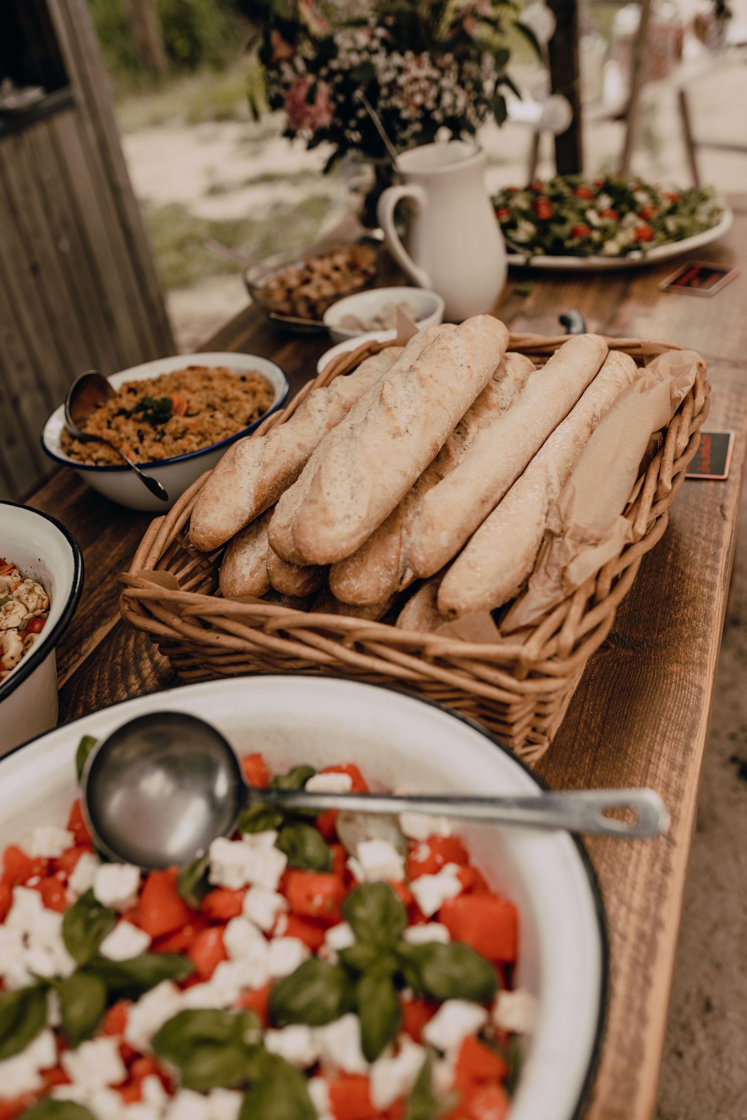 Rustic buffet spread with fresh baguettes in a basket and colorful Mediterranean salad on wooden table.