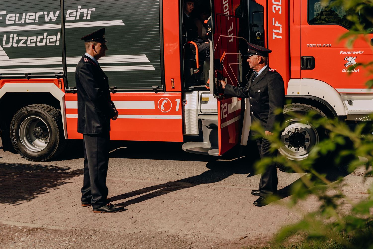 A red fire truck parked with firefighters standing beside it labeled 'Feuerwehr Utzedei'.