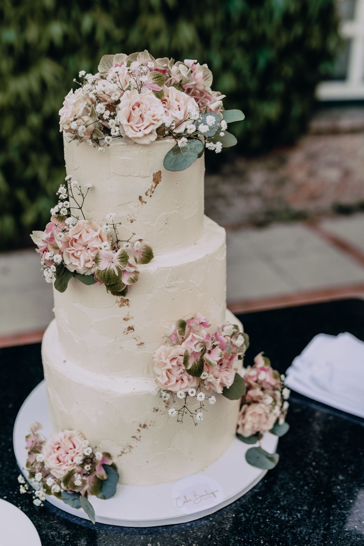 Elegant white wedding cake decorated with blush pink flowers and greenery.