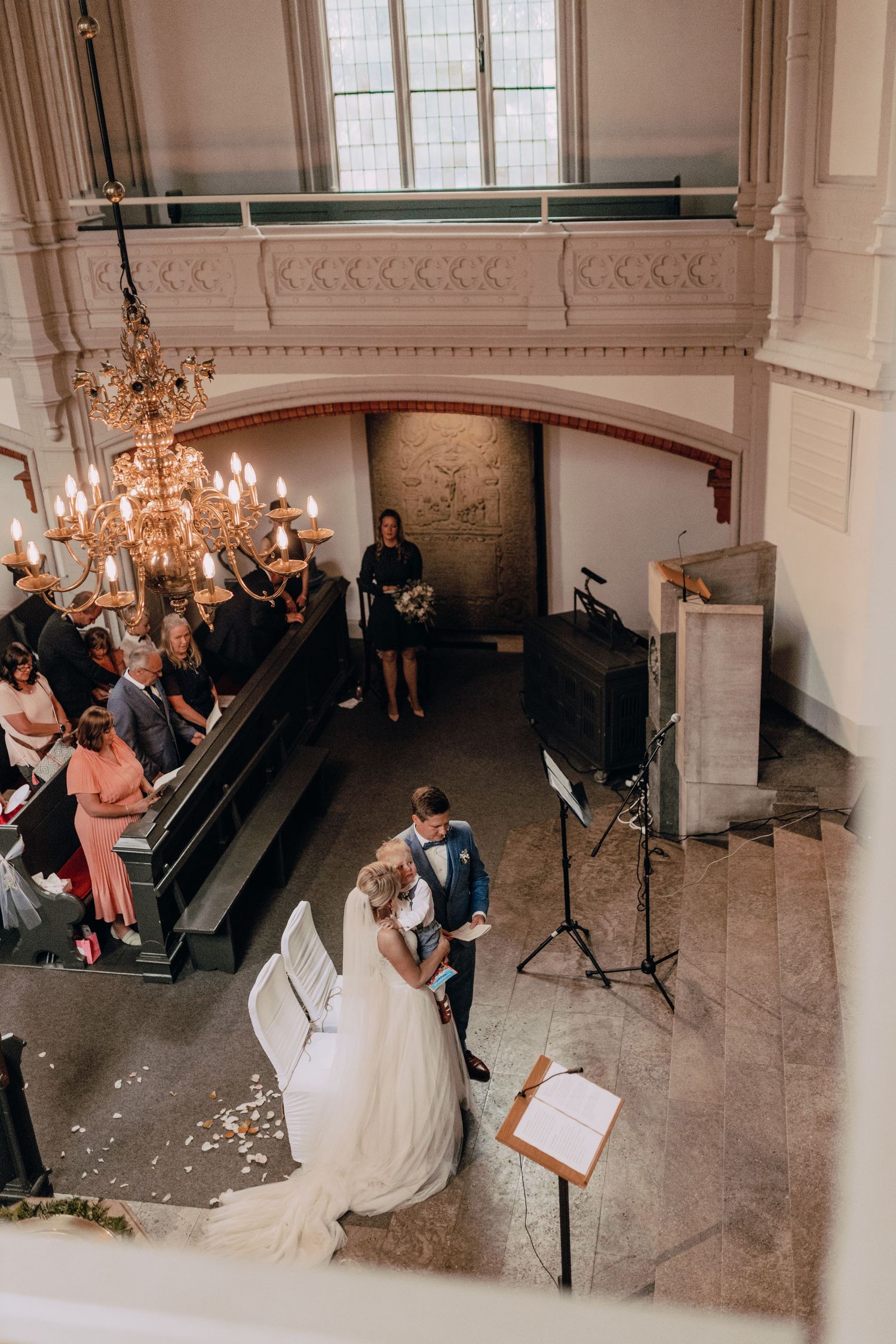 High angle view of a wedding ceremony in a grand church interior with chandelier and guests seated in wooden pews.