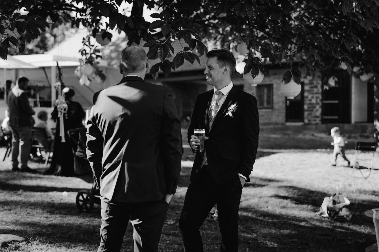 Men in formal attire conversing at an outdoor garden event in black and white.