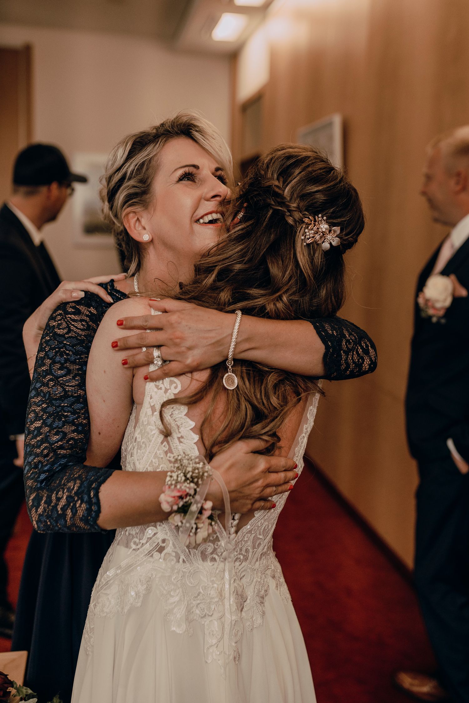 Three photos showing joyful embraces and hugs between guests at a wedding celebration in a warmly lit hallway.