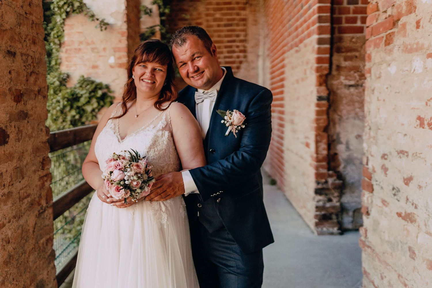 A newlywed couple posing against a rustic brick wall.