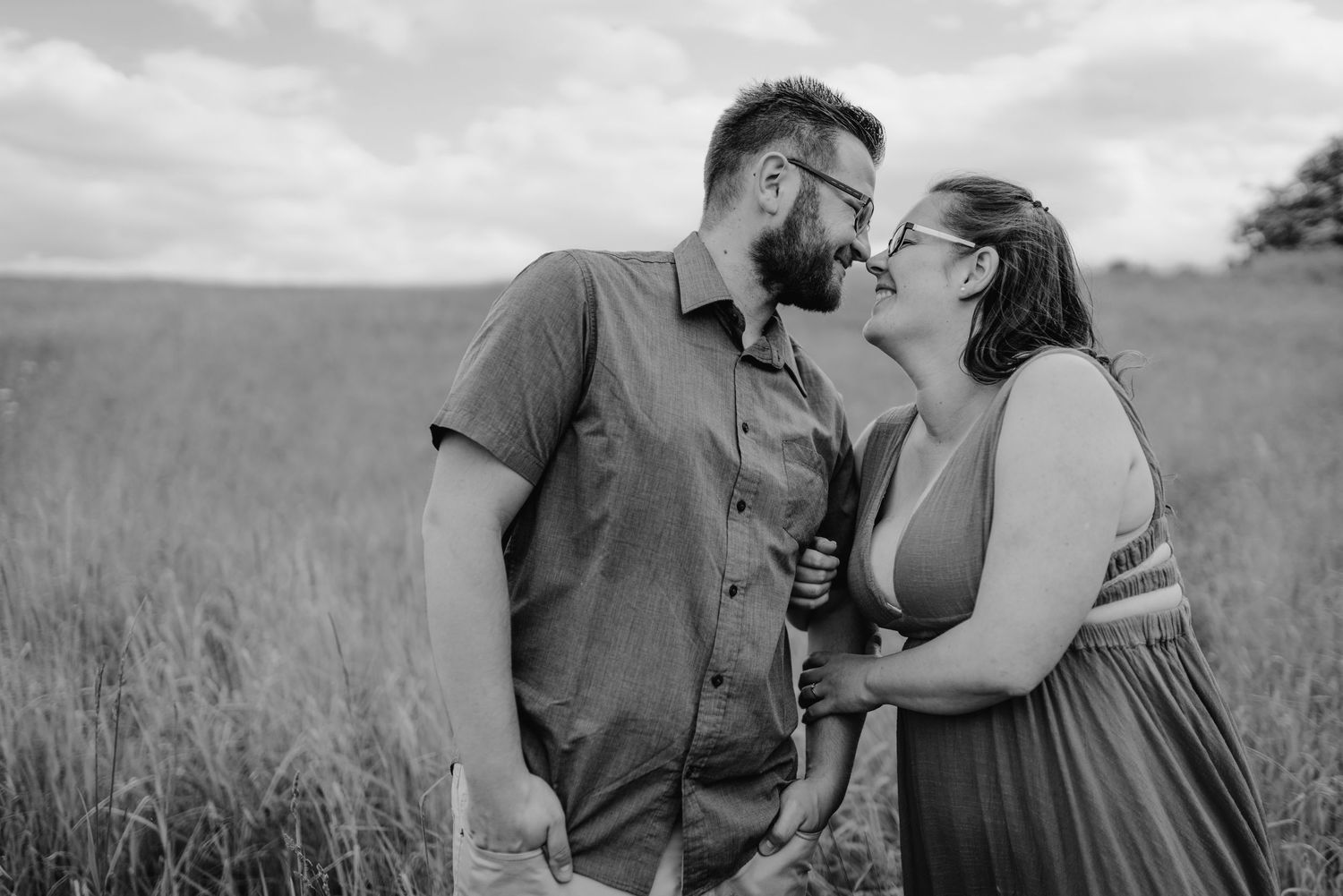 Couple embraces and kisses in a tall grassy field during an outdoor photo session at sunset.