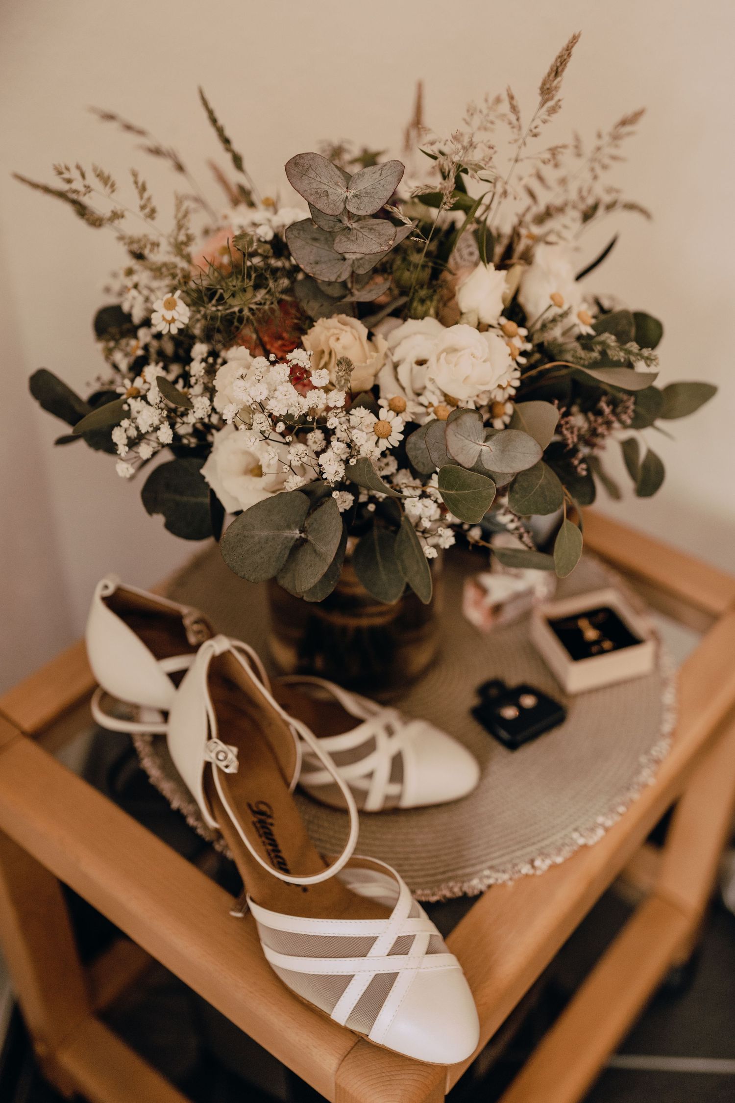 White bridal shoes and floral bouquet arranged artistically on wooden steps.