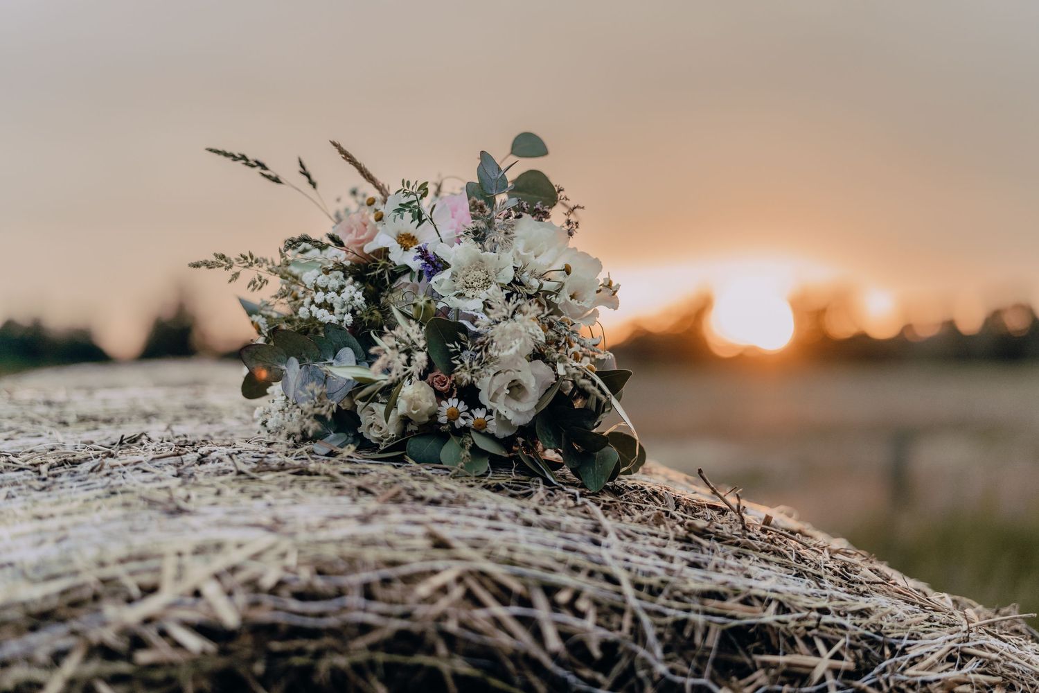 Rustic wedding bouquet with eucalyptus and white flowers against sunset horizon.