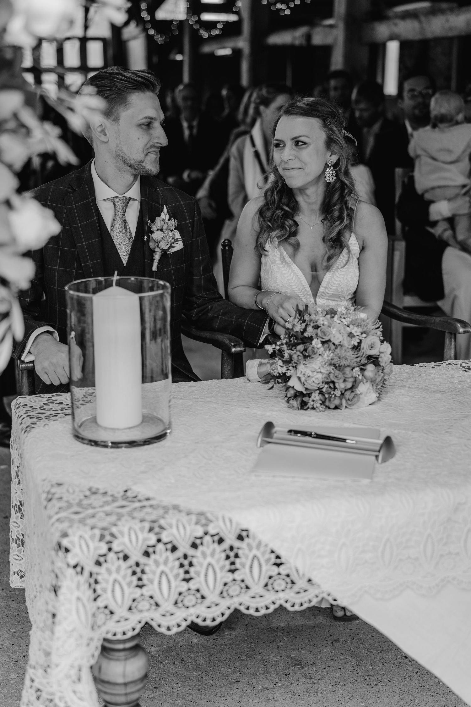 Black and white wedding reception photo showing newlyweds seated at a table with elegant lace tablecloths and candles.