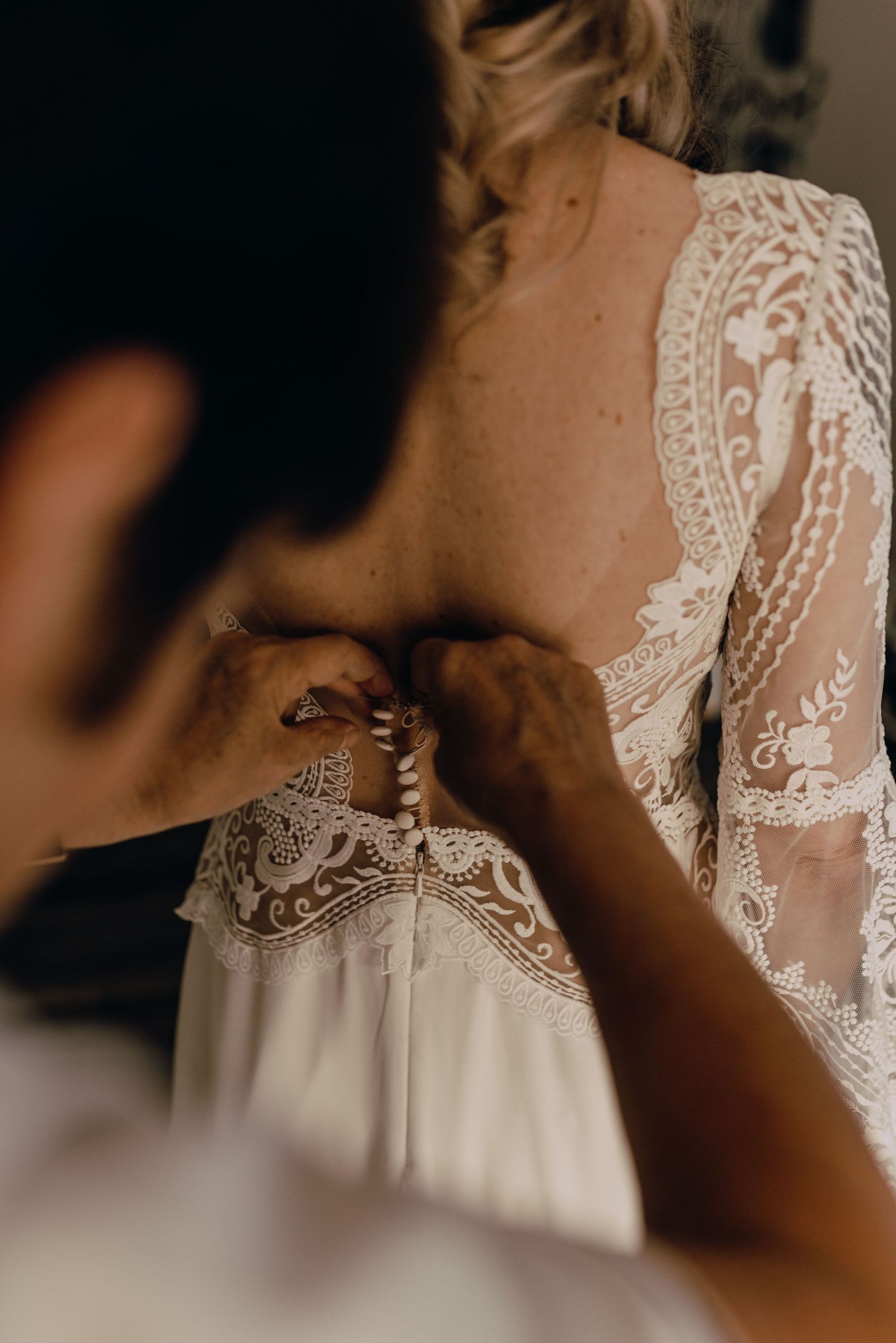 A close-up detail of delicate white lace on a wedding dress shows intricate floral patterns and sheer fabric.