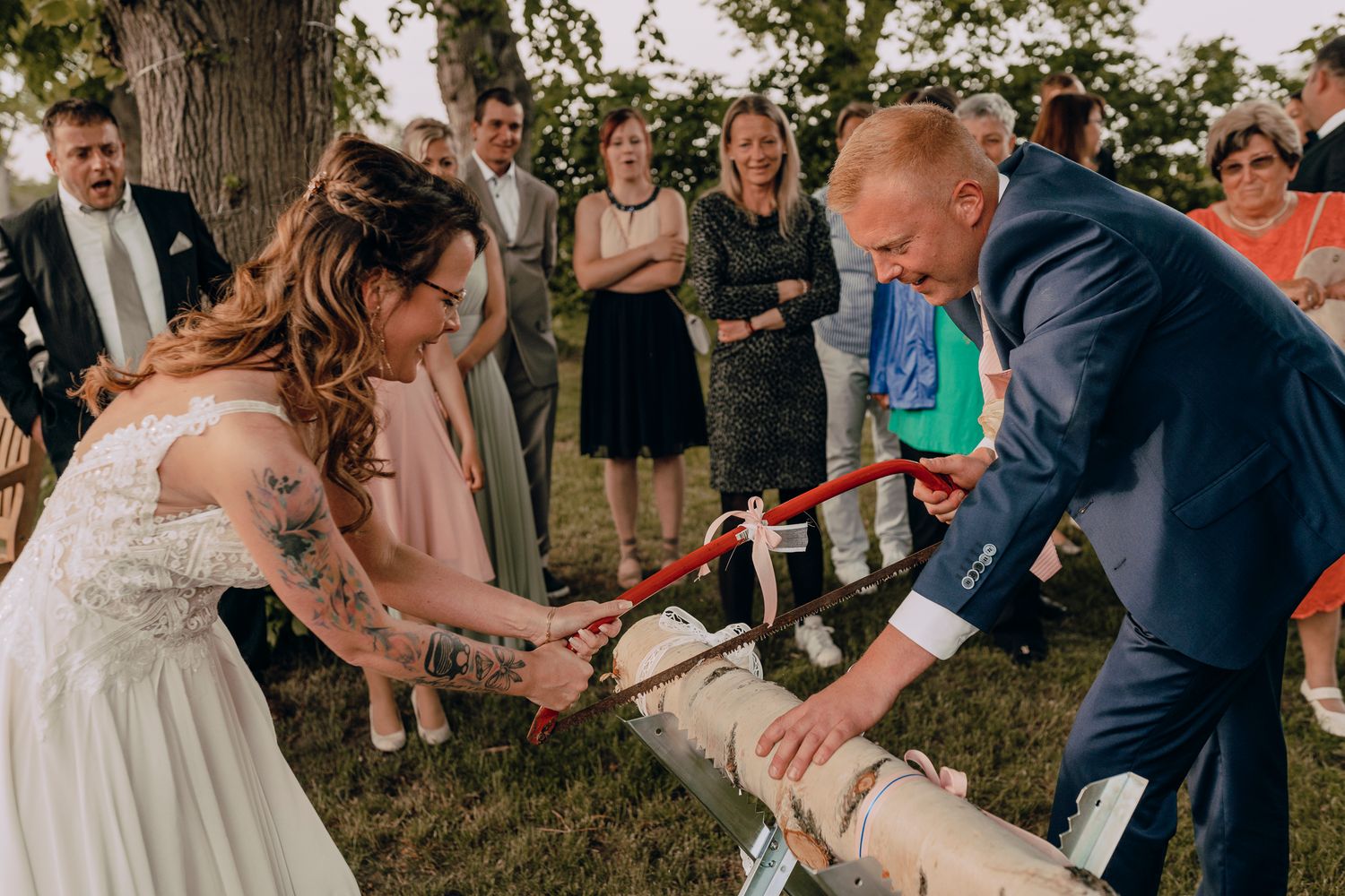 Wedding couple participates in a traditional champagne bottle opening with a sword at an outdoor celebration ceremony.